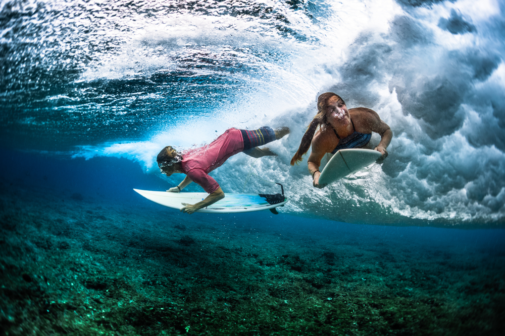 Two young surfers under a breaking wave