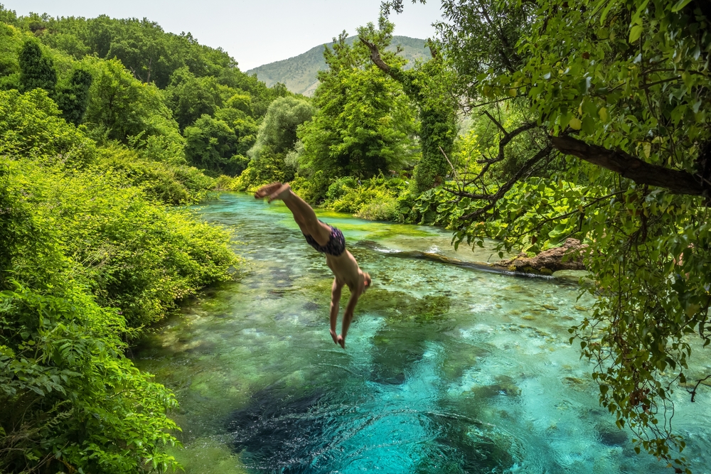 Man jumps into the beautiful turquoise spring Blue Eye