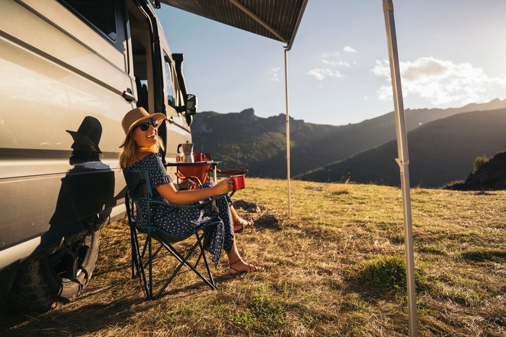 A woman chills out in a camper van and enjoys a remote retreat with a picturesque mountain landscape.